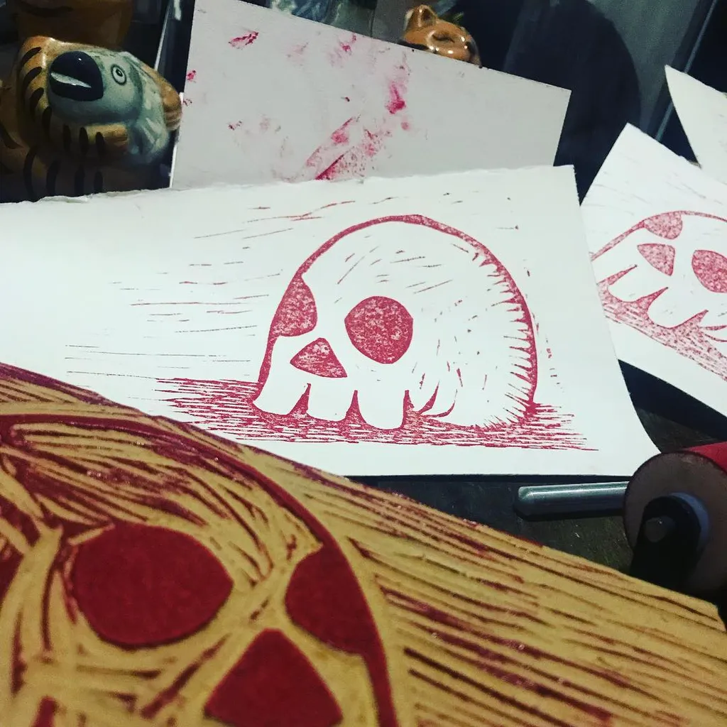 a photo of a block print and the block. the print is a skull printed in red ink.