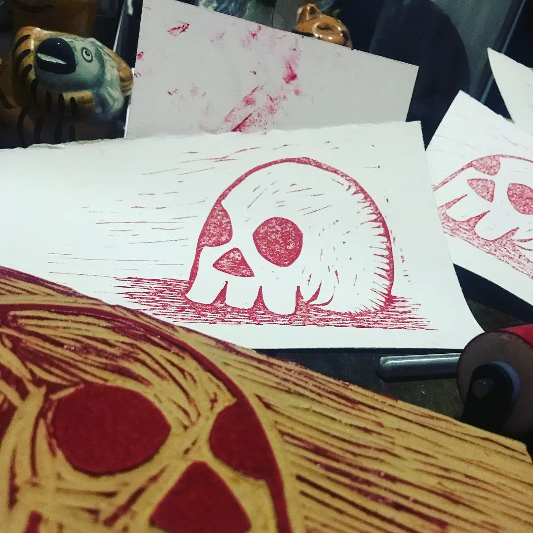 a photo of a block print and the block. the print is a skull printed in red ink.