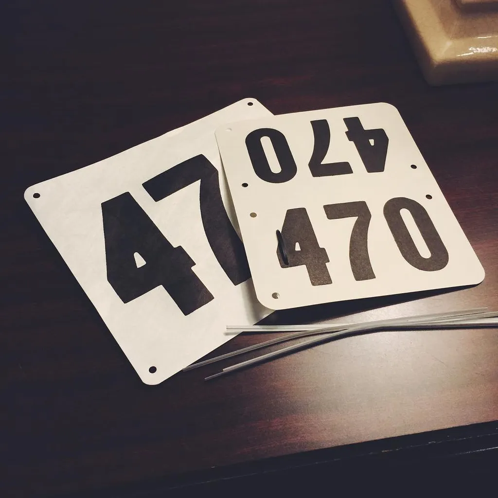 On a dark wooden surface, two white plaques featuring large black numbers 47 and 470 are positioned, with thin metallic strips scattered across the foreground.