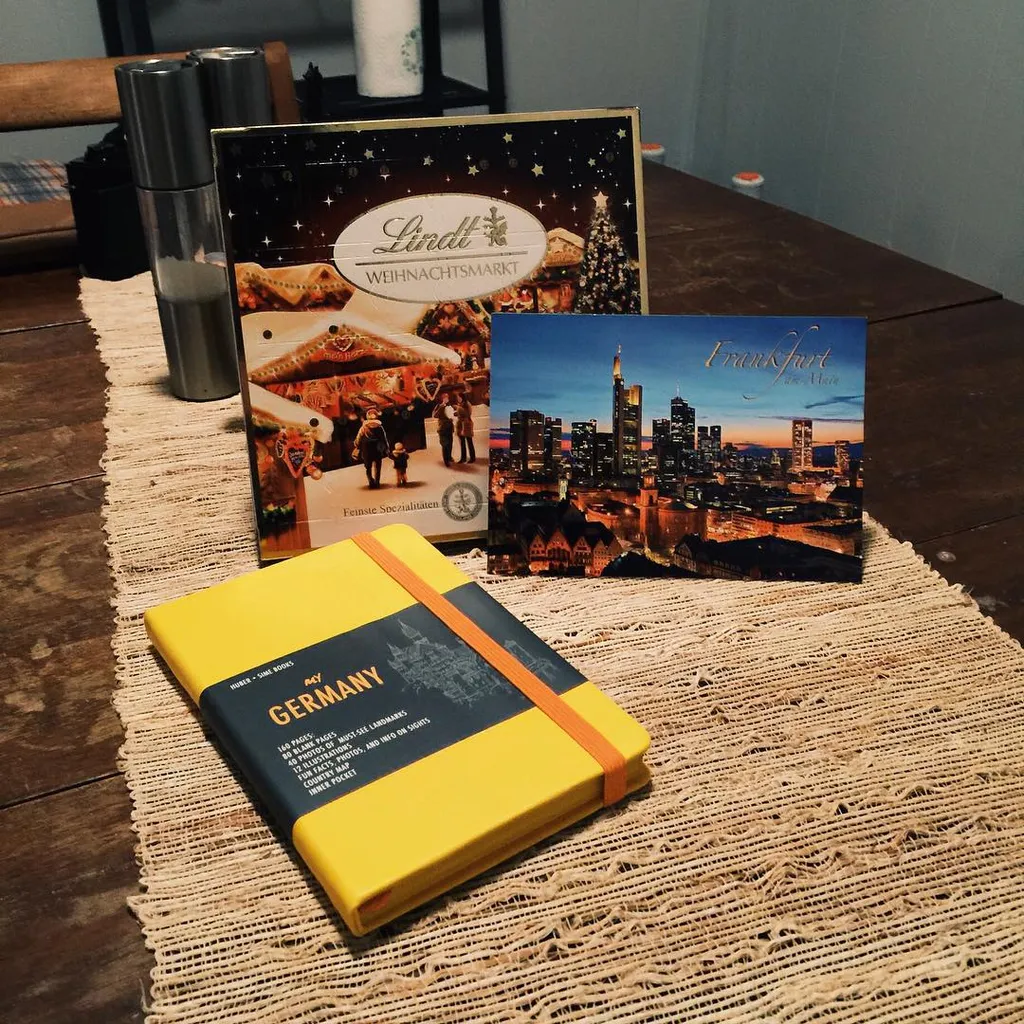 A collection of printed books and guides, featuring images of European cities and markets, rests on a woven beige mat alongside two upright metallic cylinders.