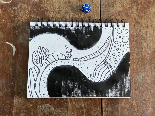A black and white sketch featuring a swirling, patterned tunnel occupies an open sketchbook resting on a wooden surface, with two dice placed on the paper.