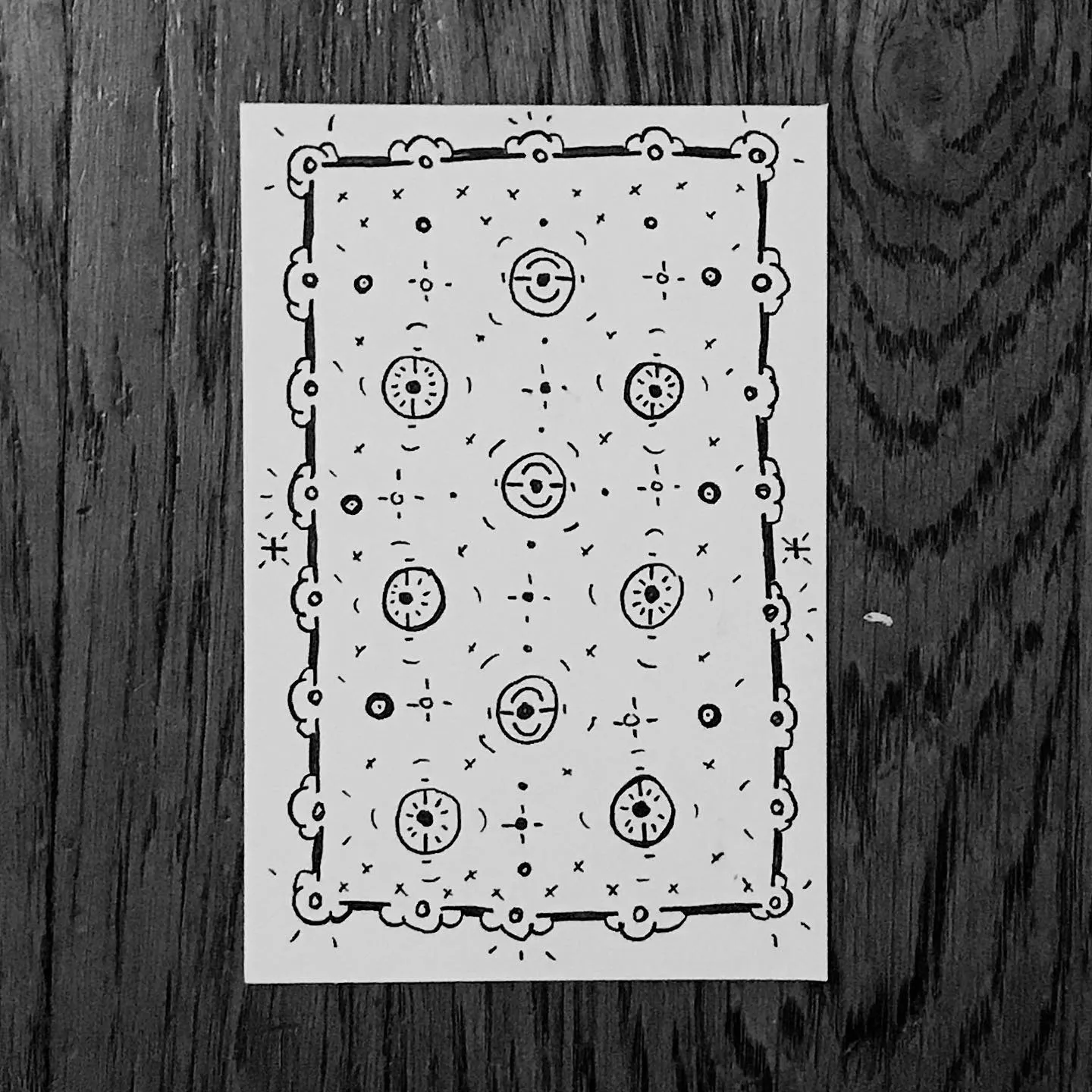 A rectangular drawing with a decorative border, filled with a dense, repeating pattern of black ink motifs, including circles, dots, and small 'x' marks.