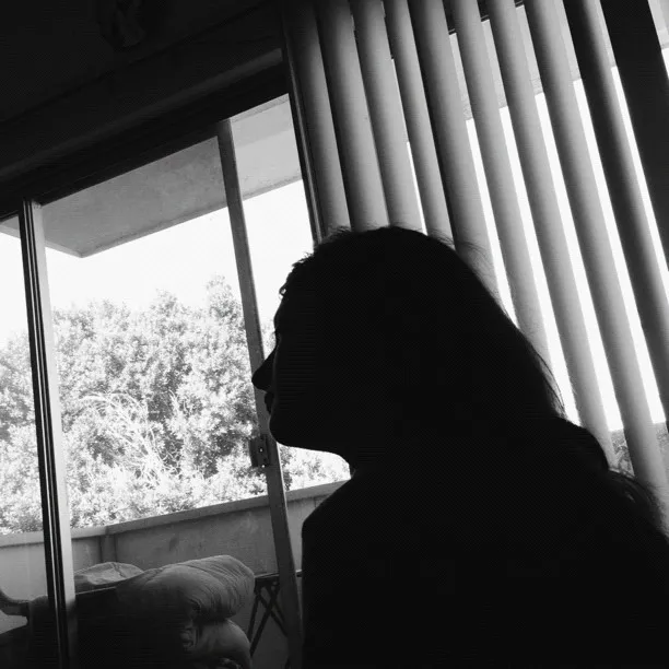 A monochrome profile silhouette of a person is set against a window view, contrasting bright outdoor foliage on the left with vertical lines of light and shadow on the right.