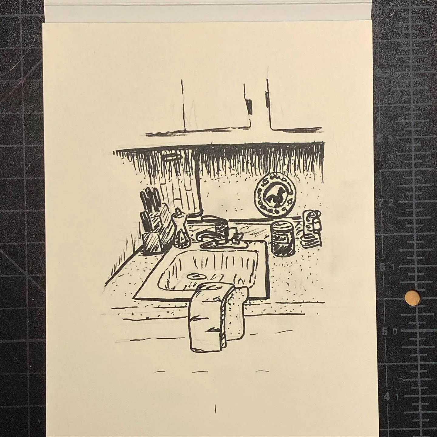 Linear black drawing depicting a simple domestic interior, showing a hearth counter with various objects and a large loaf of bread resting on the floor.