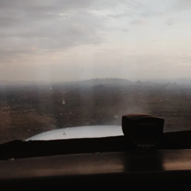 The composition features a dark foreground framing a muted landscape of pale gray and pink skies meeting a hazy horizon line and a reflective patch of water.
