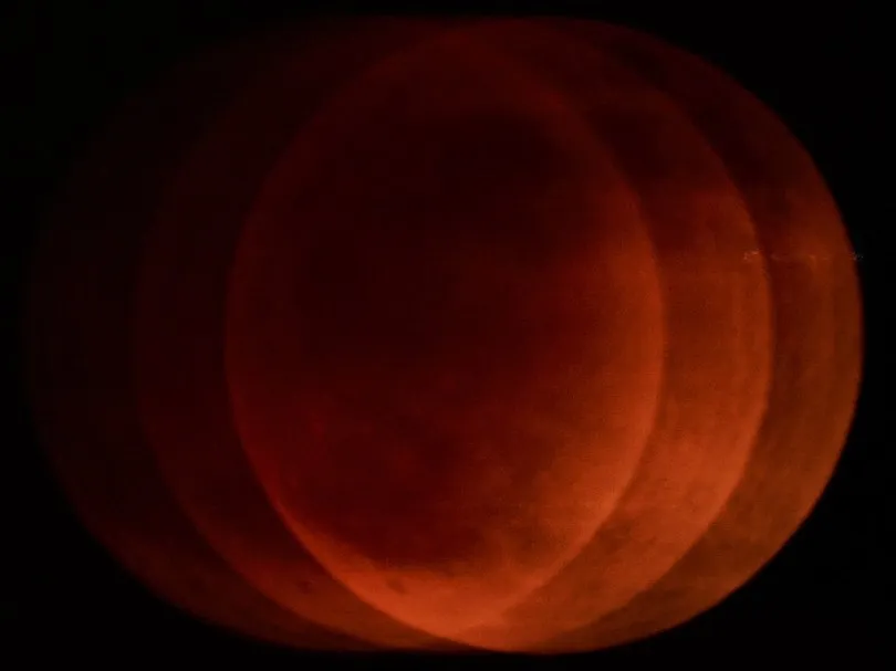 A large, circular red celestial body dominates the frame, overlaid by several overlapping, semi-circular bands of deep orange and red against a black background.
