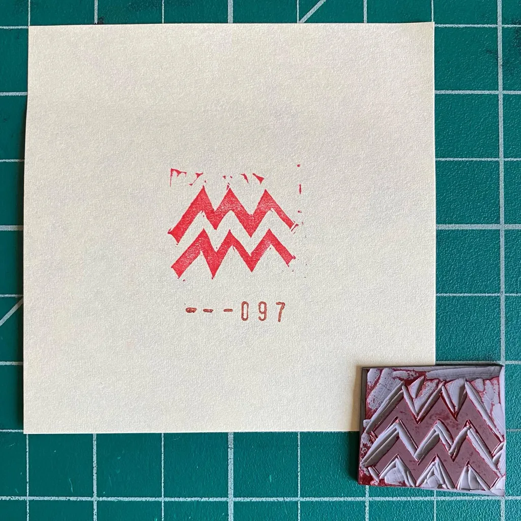 On a teal grid, a cream card displays a red zigzag motif and the number 460-097, positioned above two small rectangles featuring repeating red and white chevron patterns.