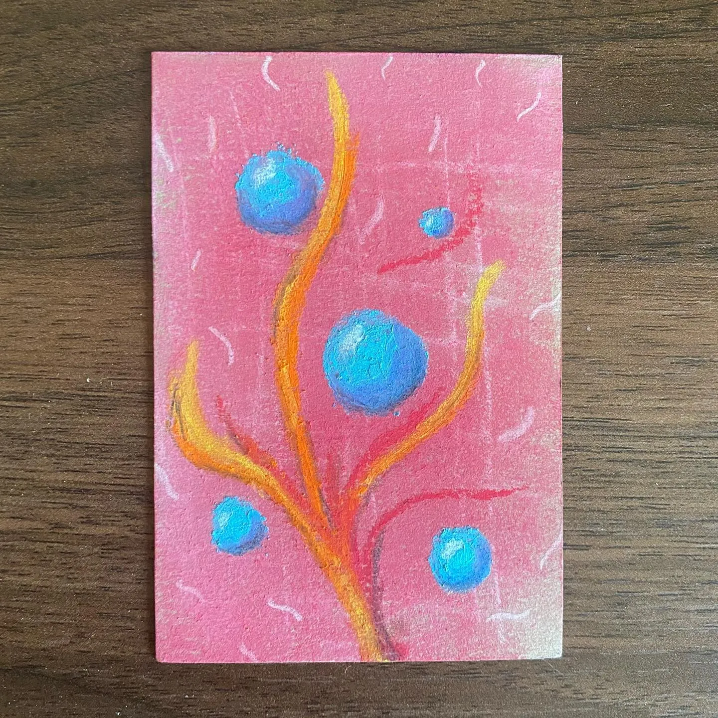 A vertical composition features stylized orange and yellow coral-like forms rising from the bottom, set against a pink background marked with white scribbles, interspersed with several bright blue circles of varying sizes.