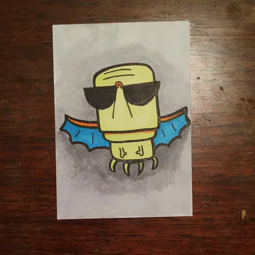 A stylized yellow creature with large black sunglasses and outstretched blue wings is drawn on white paper, surrounded by pencil shading, placed on a dark wooden surface.