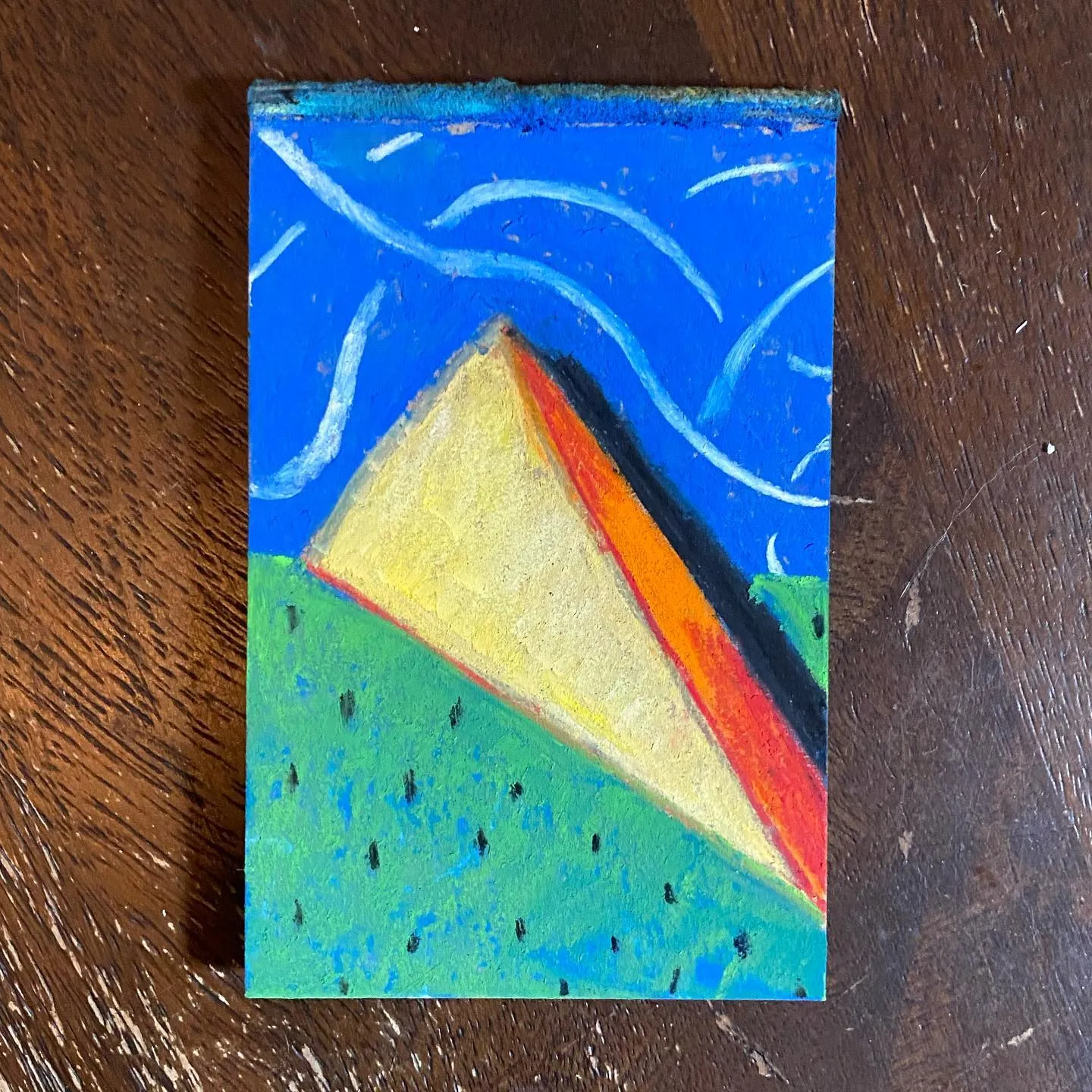 A stylized landscape features a blue sky with white wavy lines above a green foreground, dominated by a large yellow and orange triangle resting on the ground.