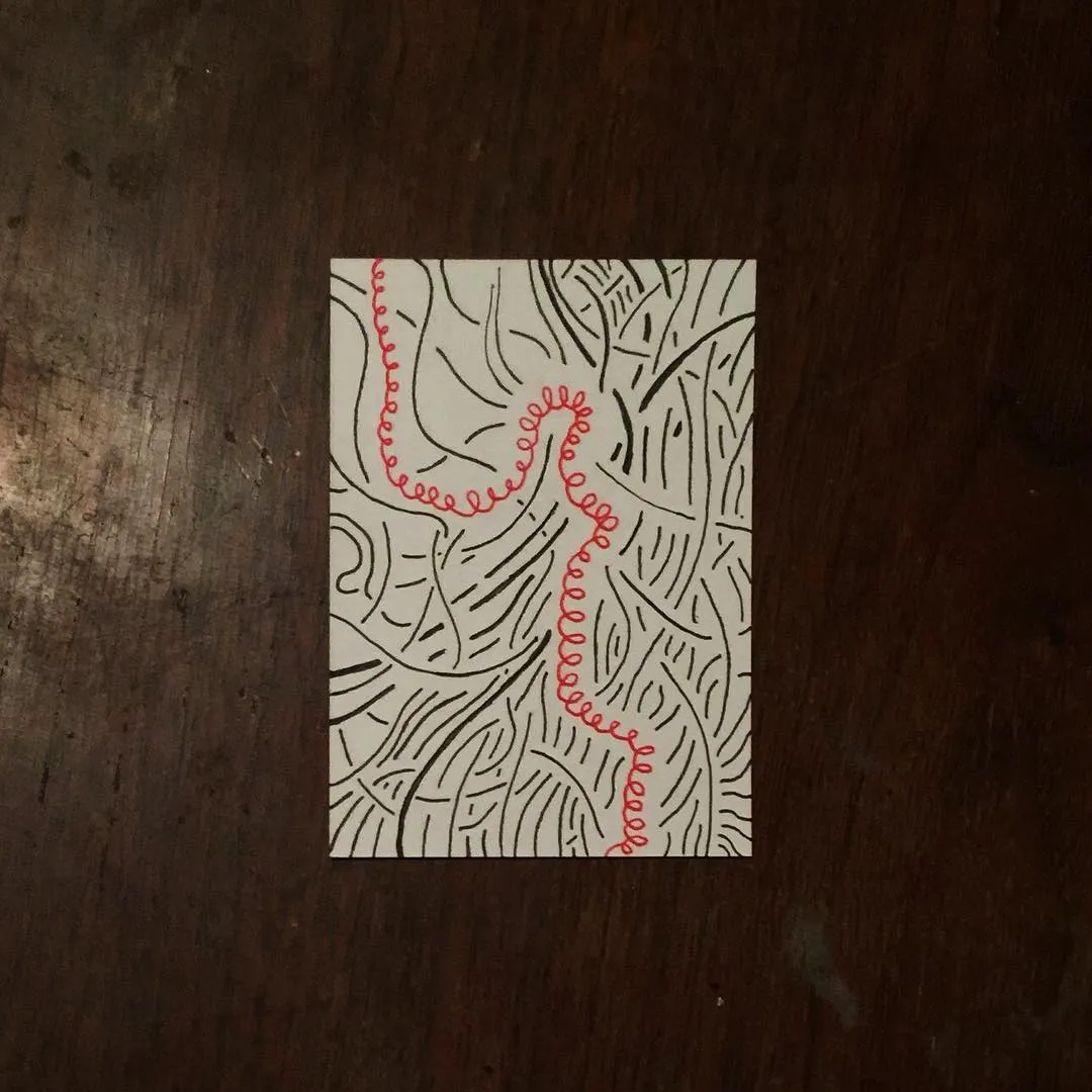 On white paper, dense black, meandering lines fill the background, creating a maze-like pattern, intersected by a prominent, wavy red line running down the center.
