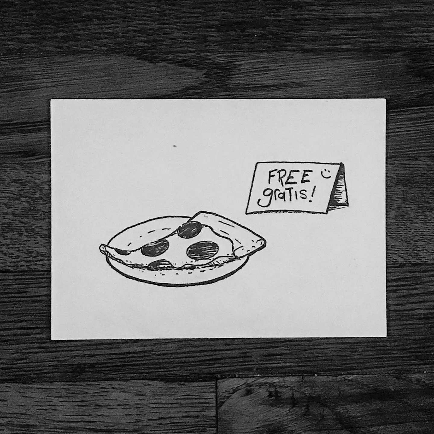 A simple black line drawing on white paper depicts a whole pizza and, to the right, a small tag with the handwritten phrase FREE gratis!