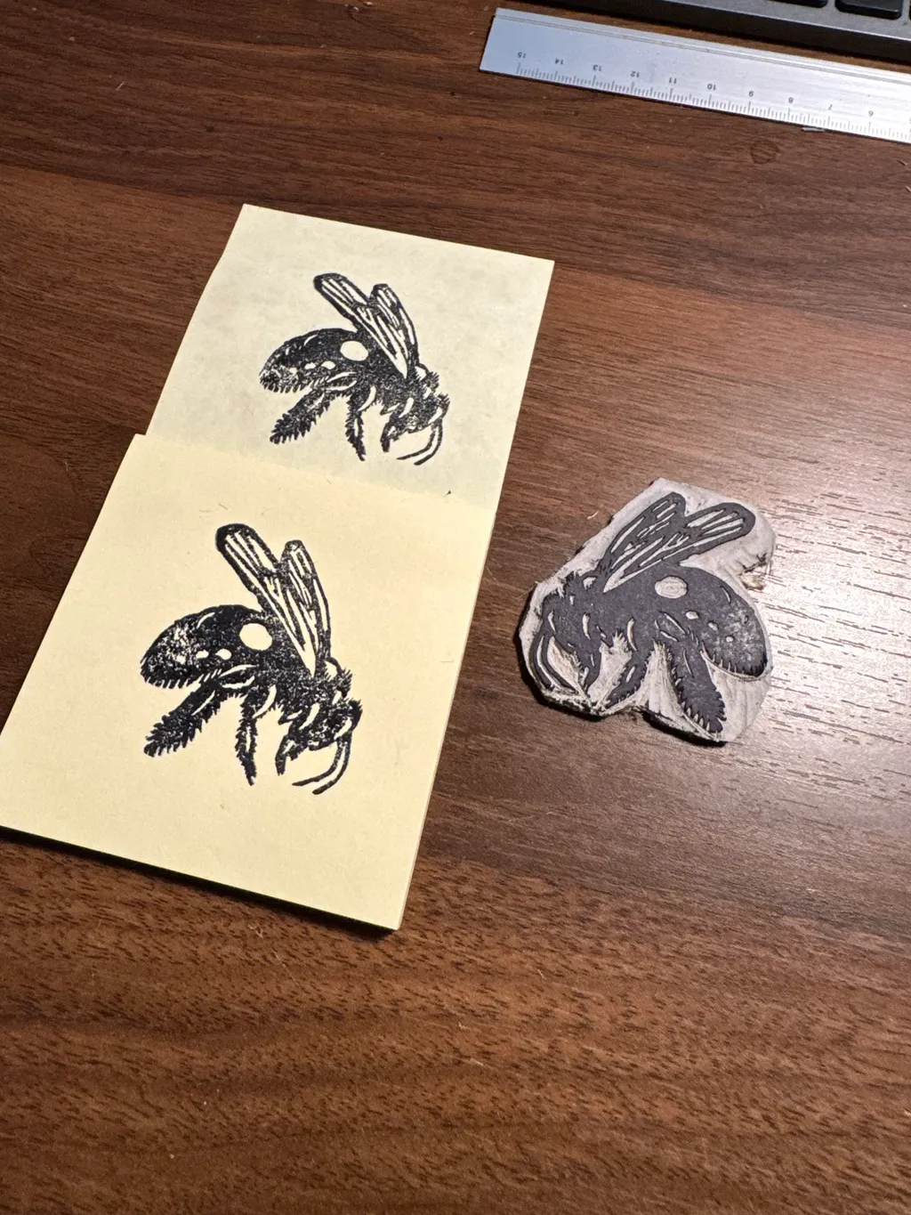 Three black ink drawings of flies are arranged on a dark wooden surface: two on yellow paper and one on a white, textured, irregular piece of material.
