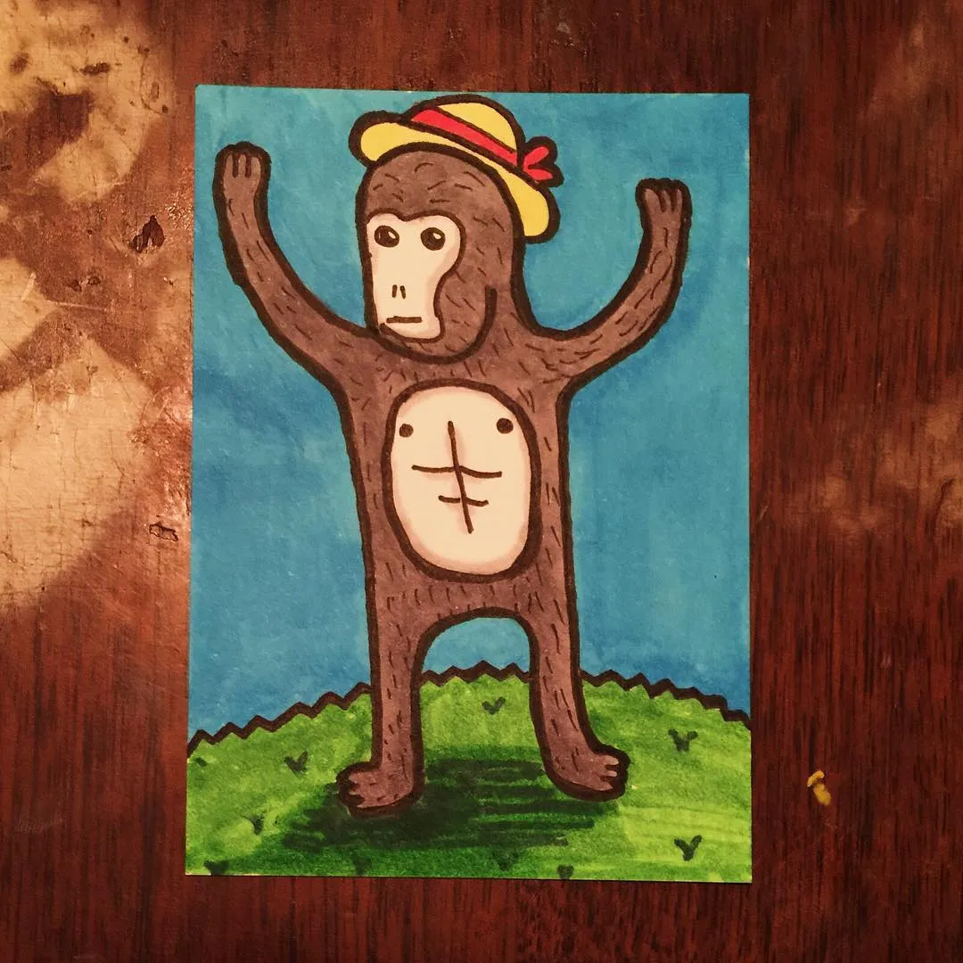 A stylized brown monkey wearing a yellow hat stands with raised arms on green grass against a bright blue background, featuring a drawn mark on its chest.