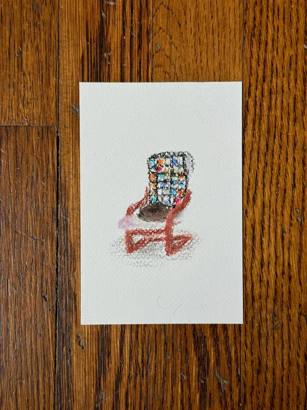 A sketch of a stylized chair featuring a multi-colored, checkered seat and reddish-brown legs, drawn on white paper against a dark, textured wood surface.