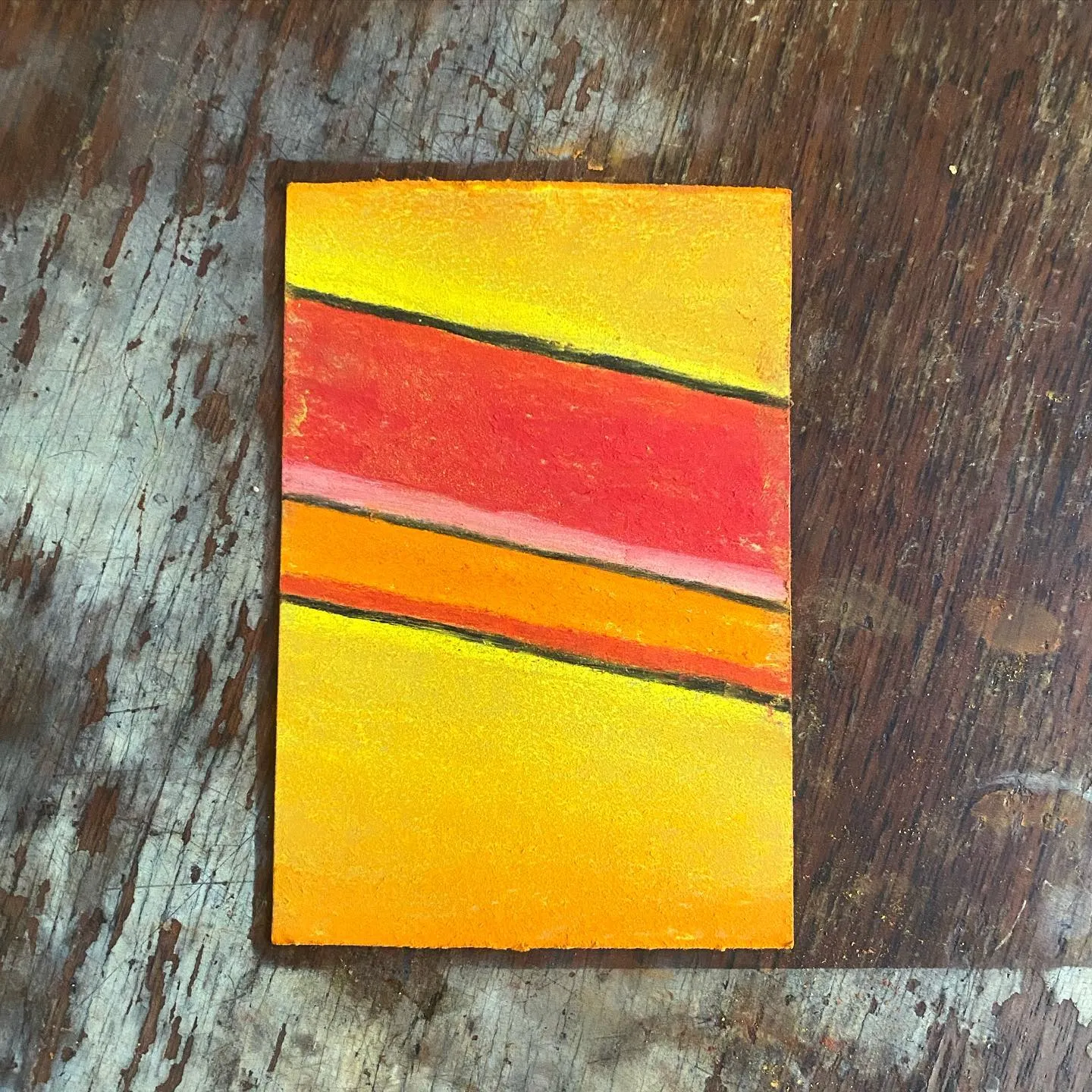 A bright yellow rectangle with three horizontal bands of red and orange stripes, set against a dark, textured wooden background.