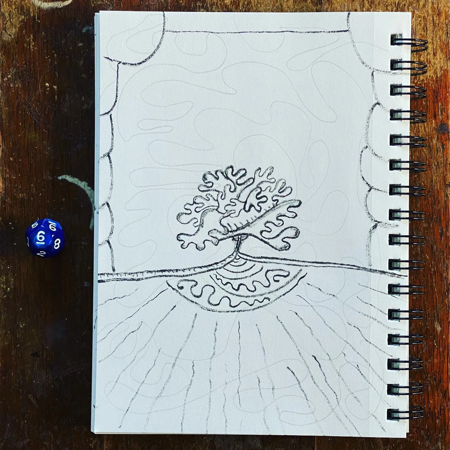 A black and white pencil drawing of a coral reef on a spiral notebook page, placed on dark wood next to a blue die marked 8.