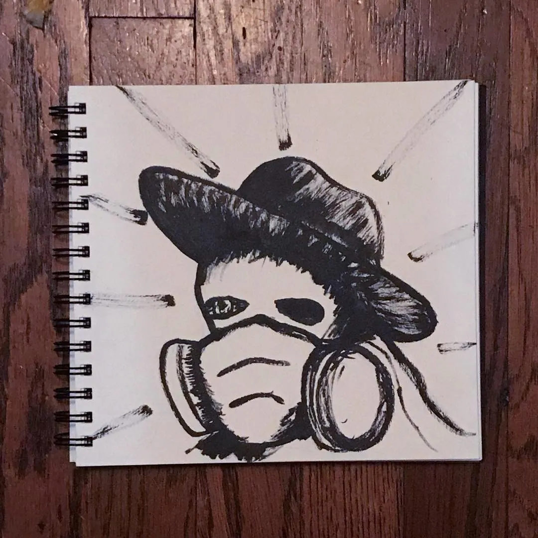 A black ink drawing on a spiral-bound sketchbook page depicts a stylized figure wearing a hat and gas mask, surrounded by radiating lines.