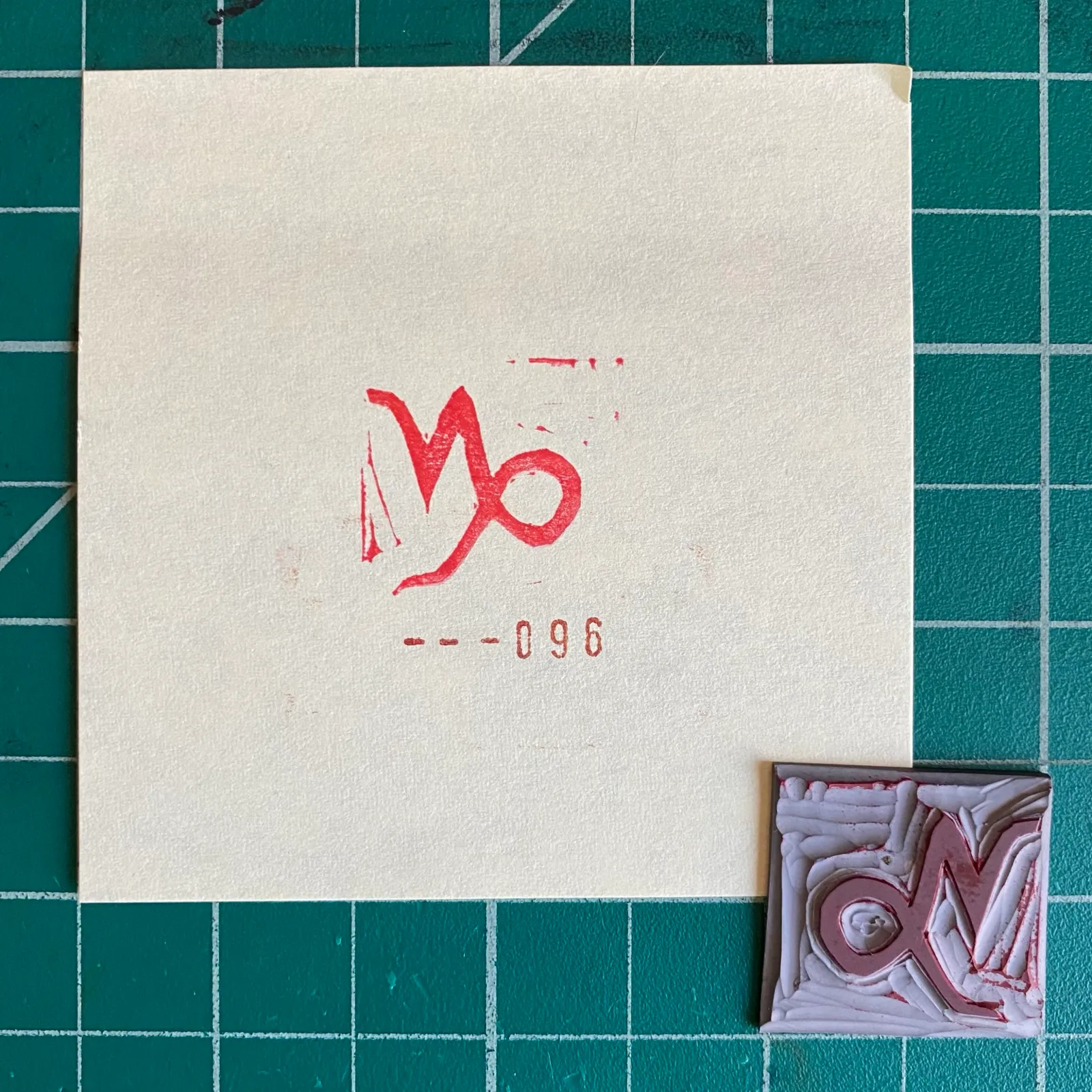 On a dark green grid background, a cream paper features a red stylized symbol and the numbers 960, next to a small square artwork with red and white layered textures.