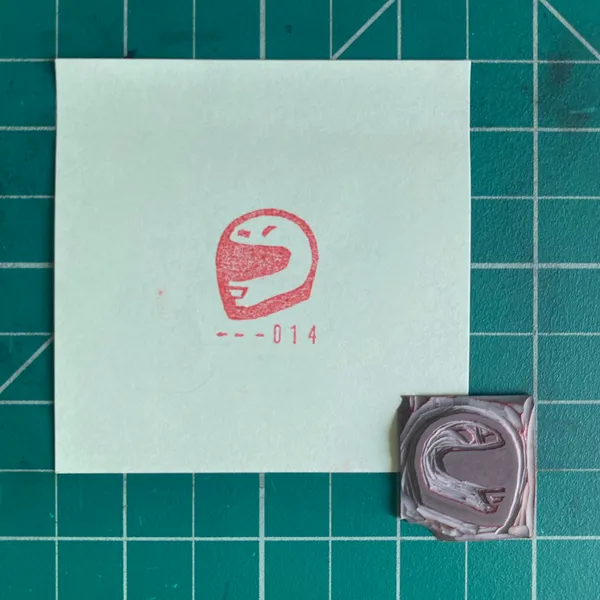 A white card on a teal grid features a red stylized face and the number 014, positioned above two small, layered squares of brown and mauve material.