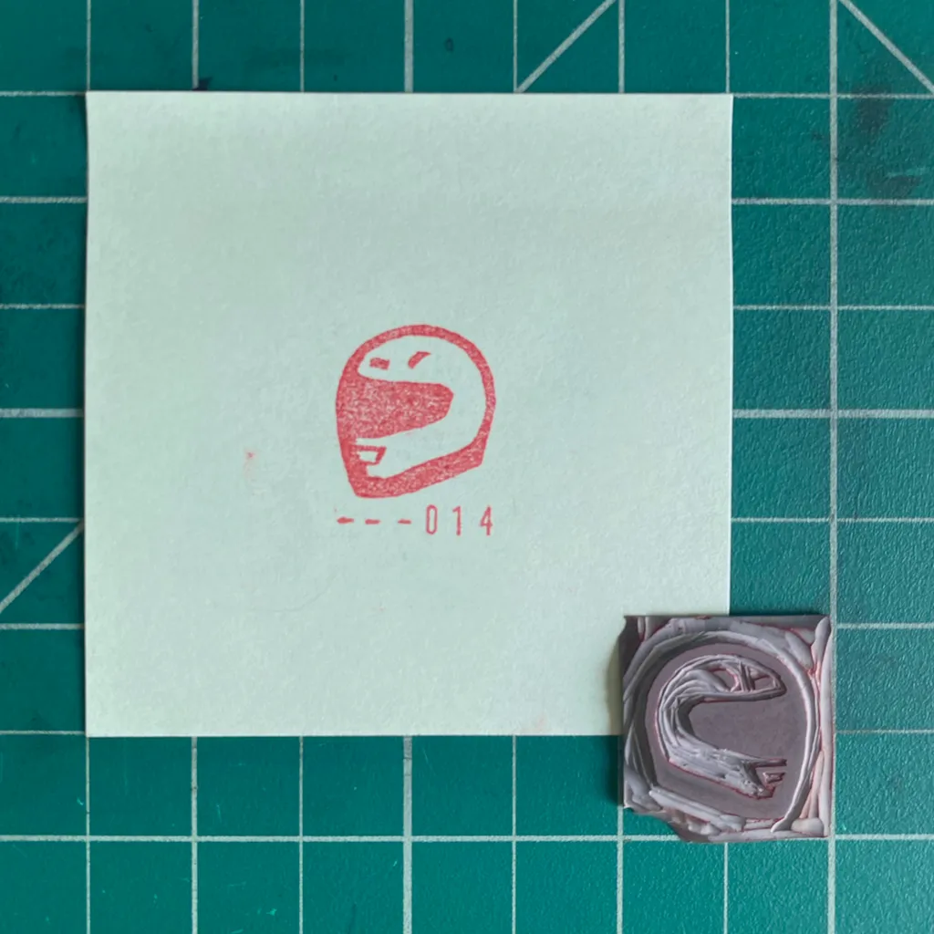 A white card on a teal grid features a red stylized face and the number 014, positioned above two small, layered squares of brown and mauve material.