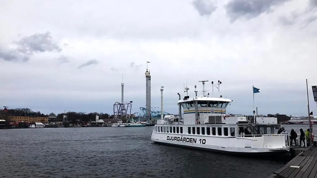 A large white boat labeled DJURGÅRDEN 10 docks on the right, set against a dark harbor and a distant industrial skyline under a heavy, overcast gray sky.