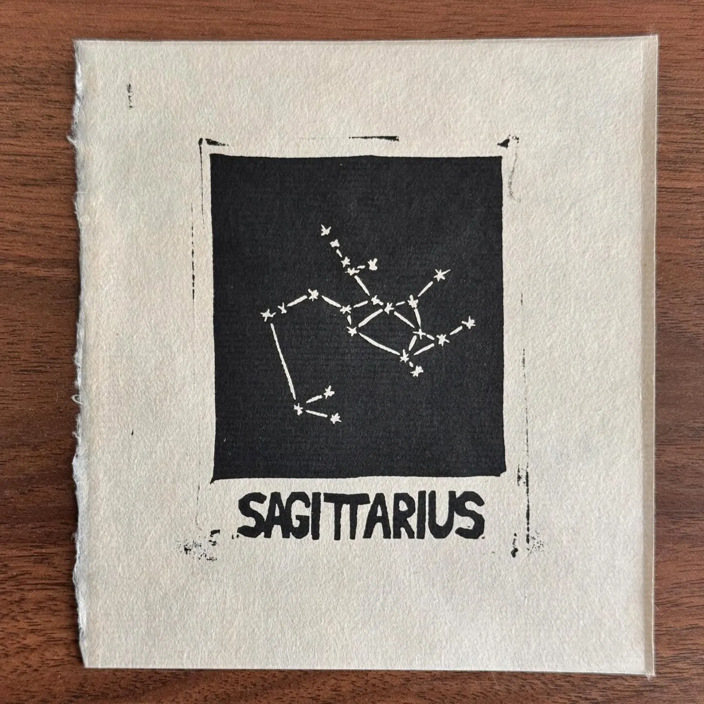 A dark square patch contains a white line-drawn constellation diagram of Sagittarius, with the name SAGITTARIUS printed in large letters beneath the square on the off-white paper.