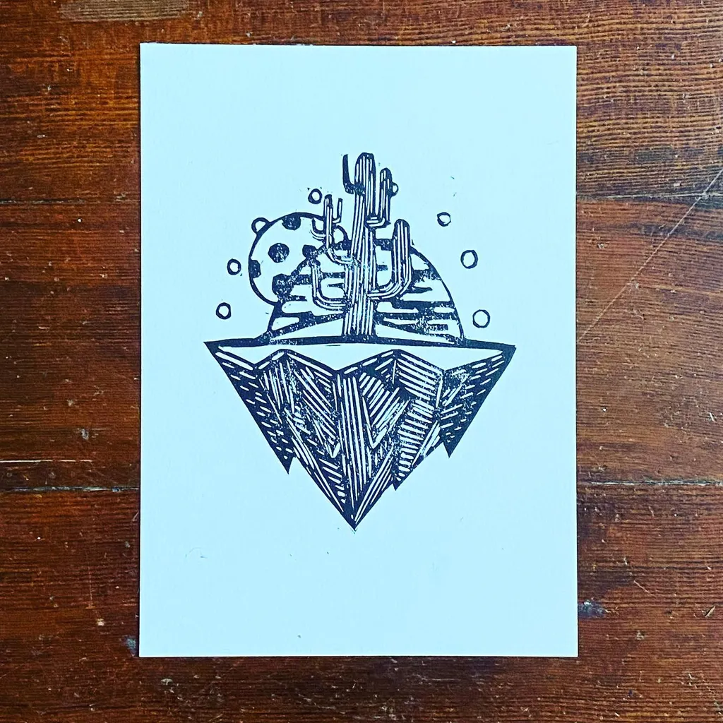 A black line drawing on light paper depicts saguaro cacti and a round cactus emerging from a geometric, patterned base, set on a dark wooden surface.