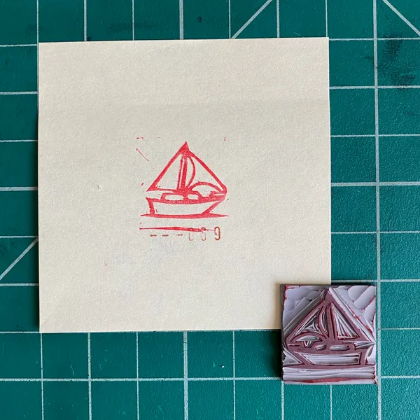 On a cream background, a red line drawing of a sailboat sits above a small, folded piece of art featuring layered pink and gray geometric shapes.
