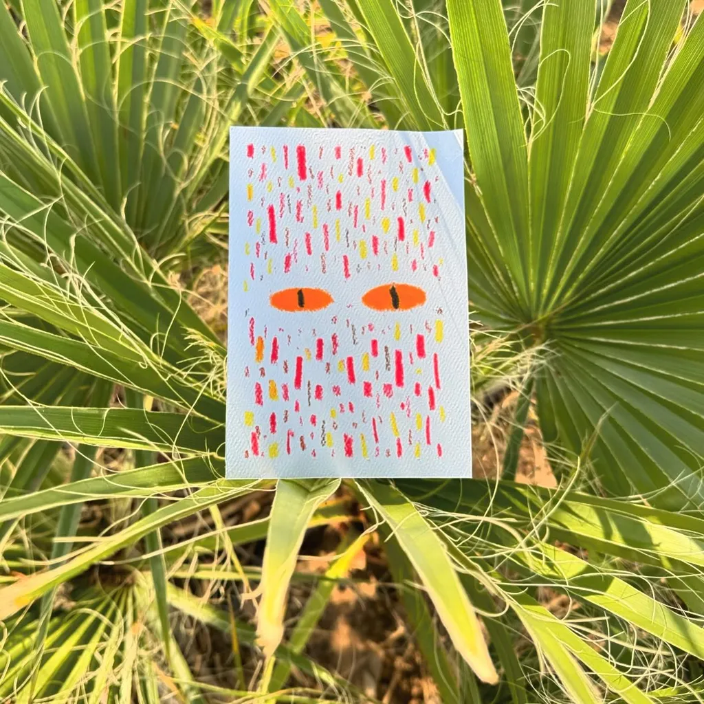 A small card featuring two orange eyes and a pattern of colorful vertical dashes is centered among lush, bright green, tropical foliage.