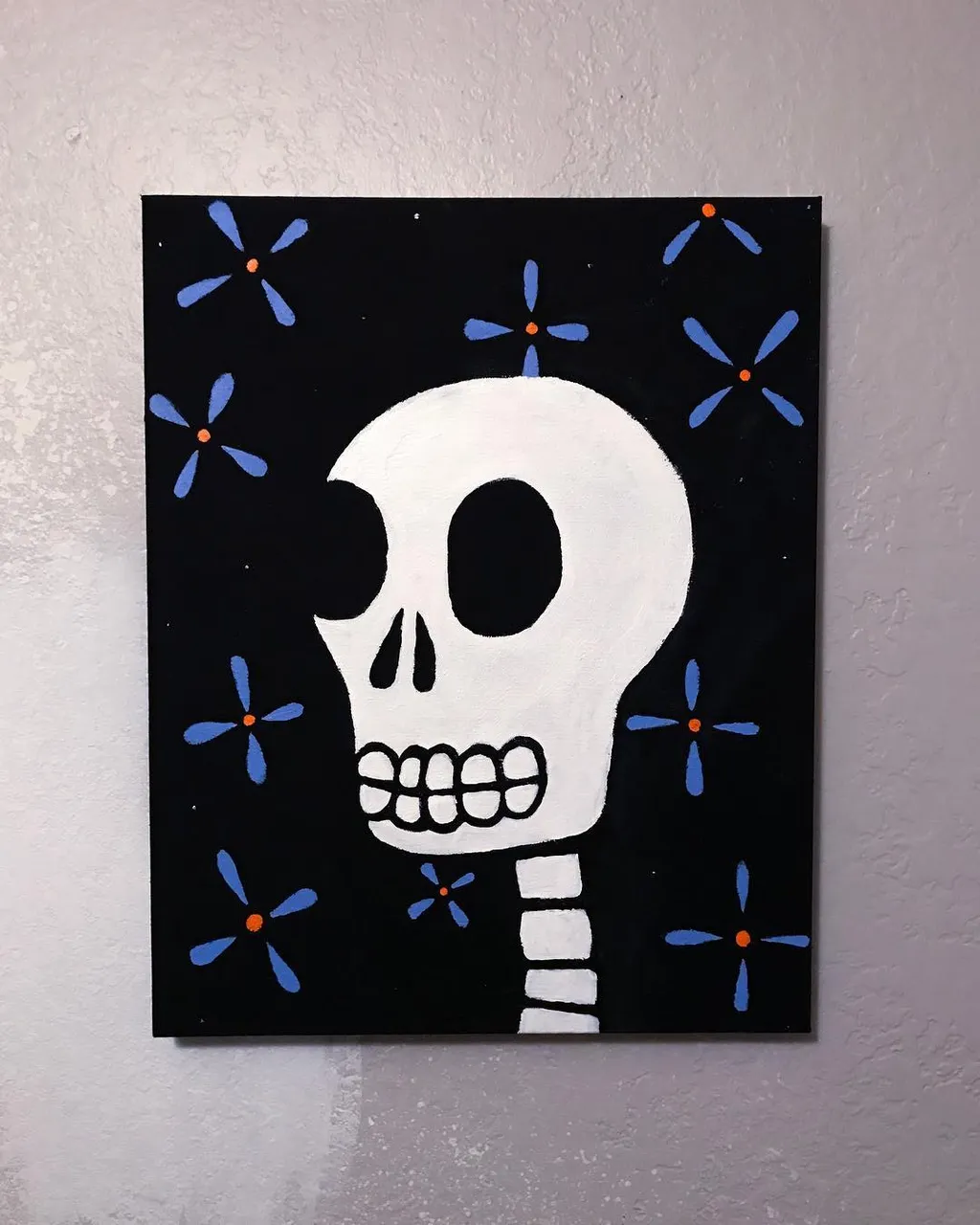 A stylized white skull with a visible spine dominates the center of a black square, surrounded by scattered blue and orange floral motifs.