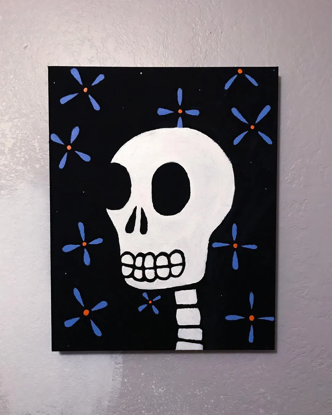 A stylized white skull with a visible spine dominates the center of a black square, surrounded by scattered blue and orange floral motifs.