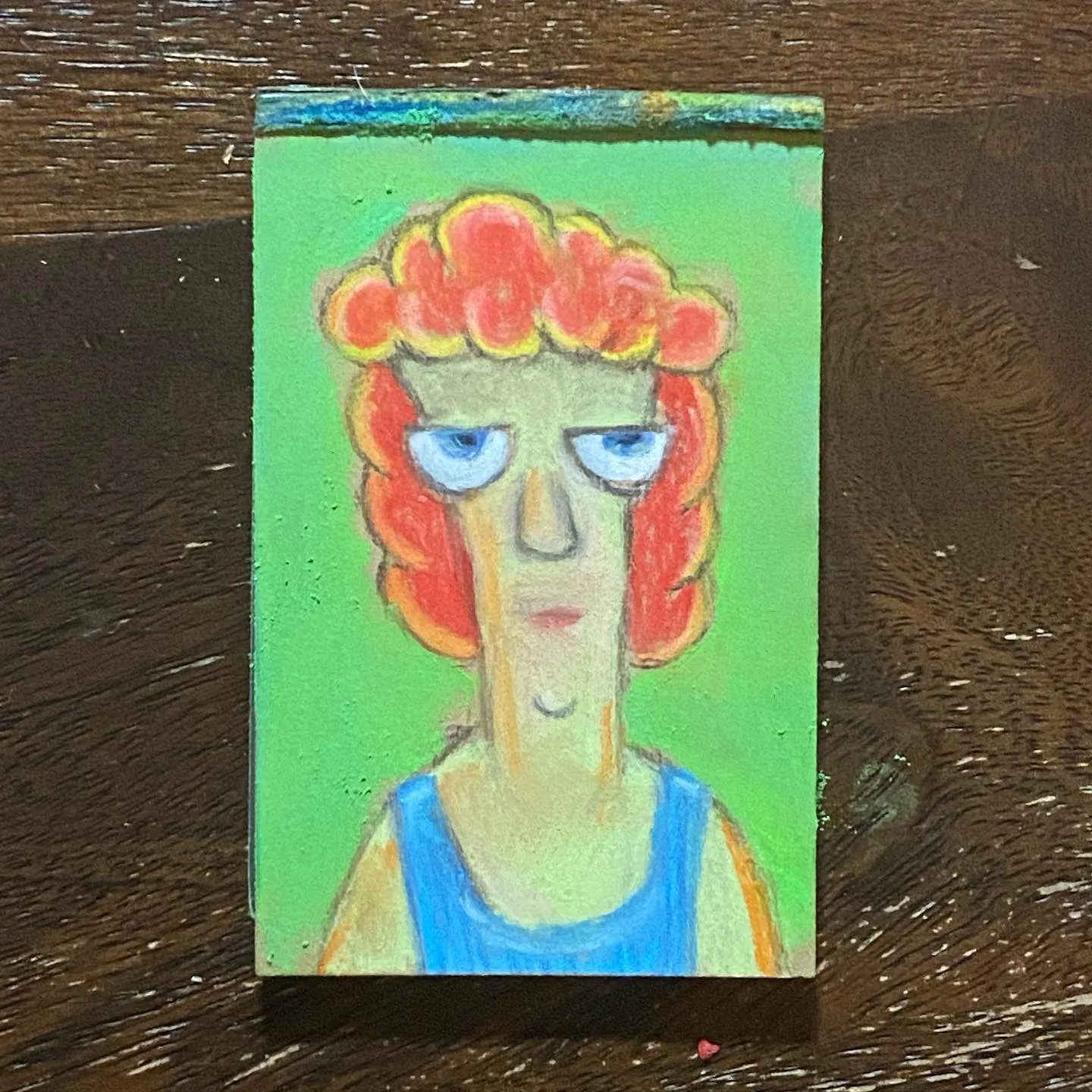 A stylized portrait features a figure with bright red hair and a blue top, painted on a vibrant green background, showing pale skin and large, expressive blue eyes.