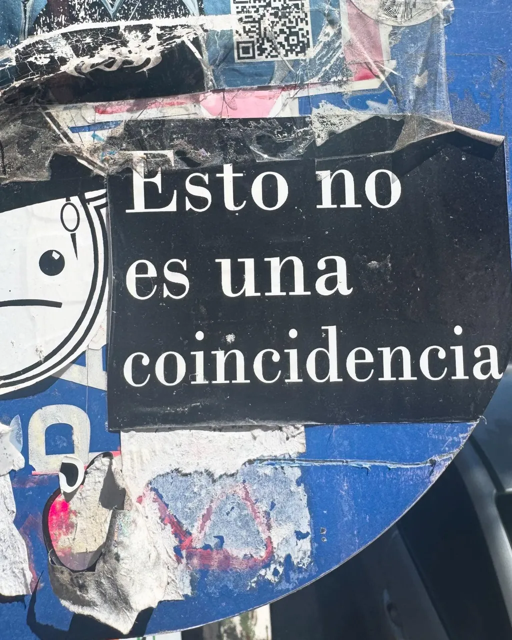 White text on a black rectangle reads Esto no es una coincidencia, set against a heavily distressed blue background with peeling paint and a partial cartoon face drawing on the left.