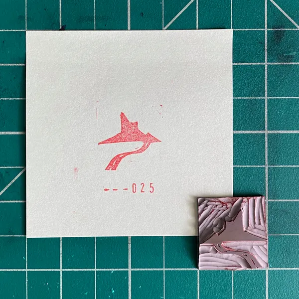 A white card on a teal grid displays a red stylized figure and the number --025, next to a small rectangular piece with marbled pink, white, and gray textures.
