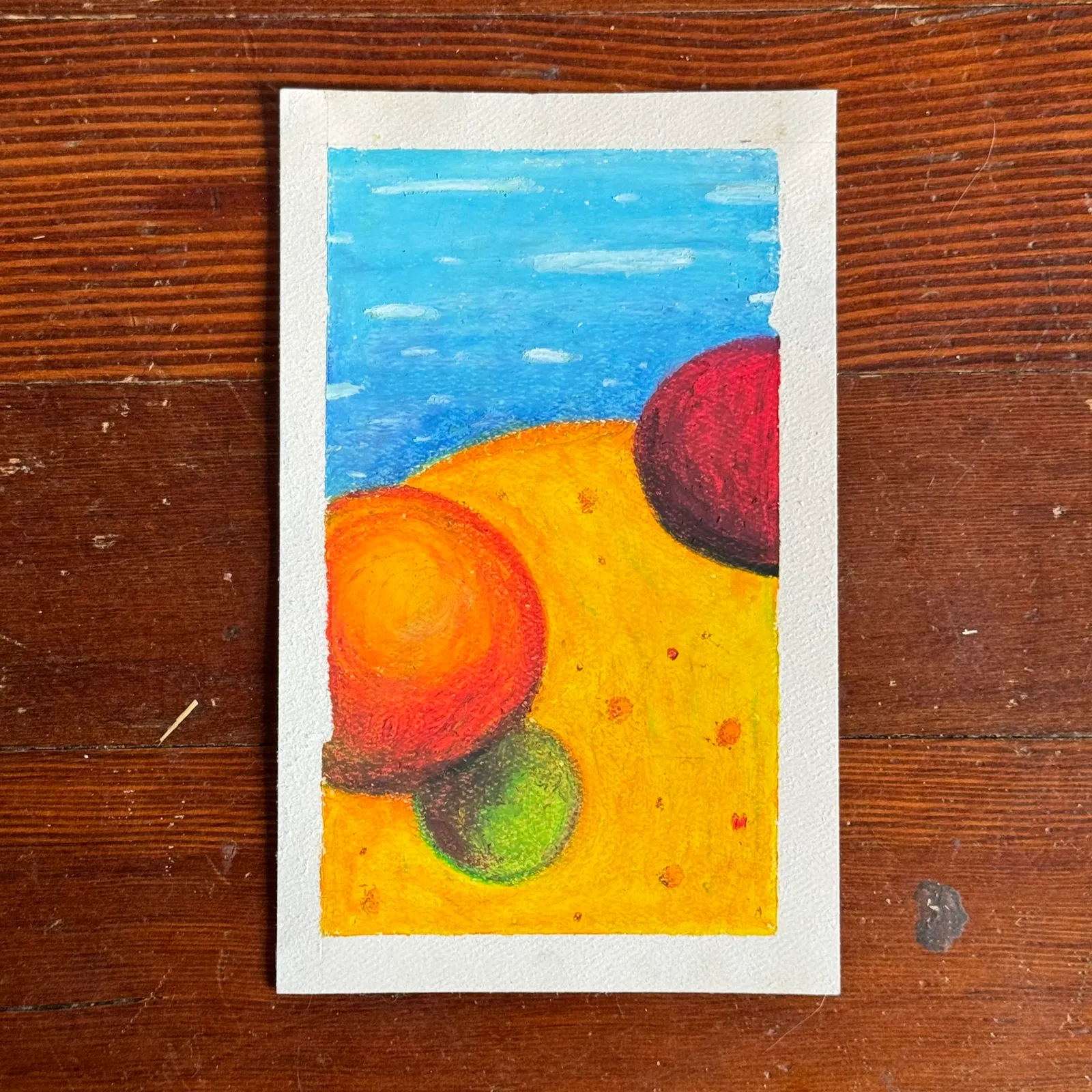 A stylized landscape composition shows a blue sky above a yellow ground, containing three overlapping, brightly colored circular shapes: red, orange, and green.