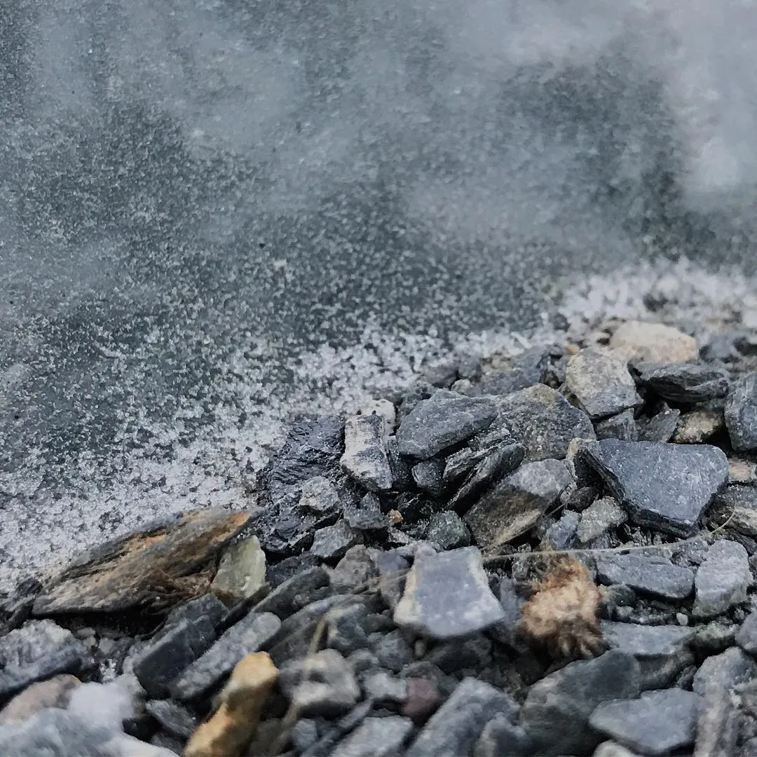 Angular gray and brown gravel fills the bottom foreground, partially covered by a dense, light gray cloud of fine dust that drifts across the upper half of the frame.