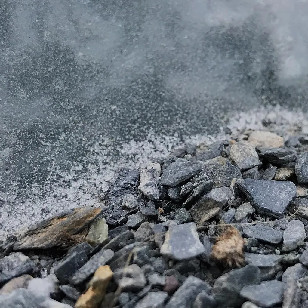 Angular gray and brown gravel fills the bottom foreground, partially covered by a dense, light gray cloud of fine dust that drifts across the upper half of the frame.