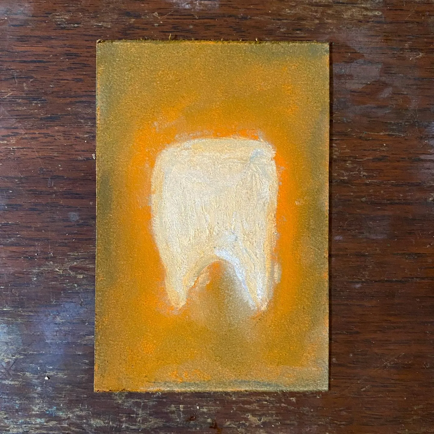 A golden, textured tooth is centered on a square background that glows brightly, fading into a darker ochre gold, all resting on a dark wooden surface.