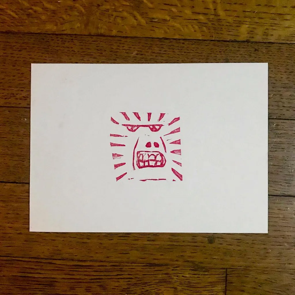 A red drawing of a stylized, aggressive face with teeth and radiating lines is centered on a white card.