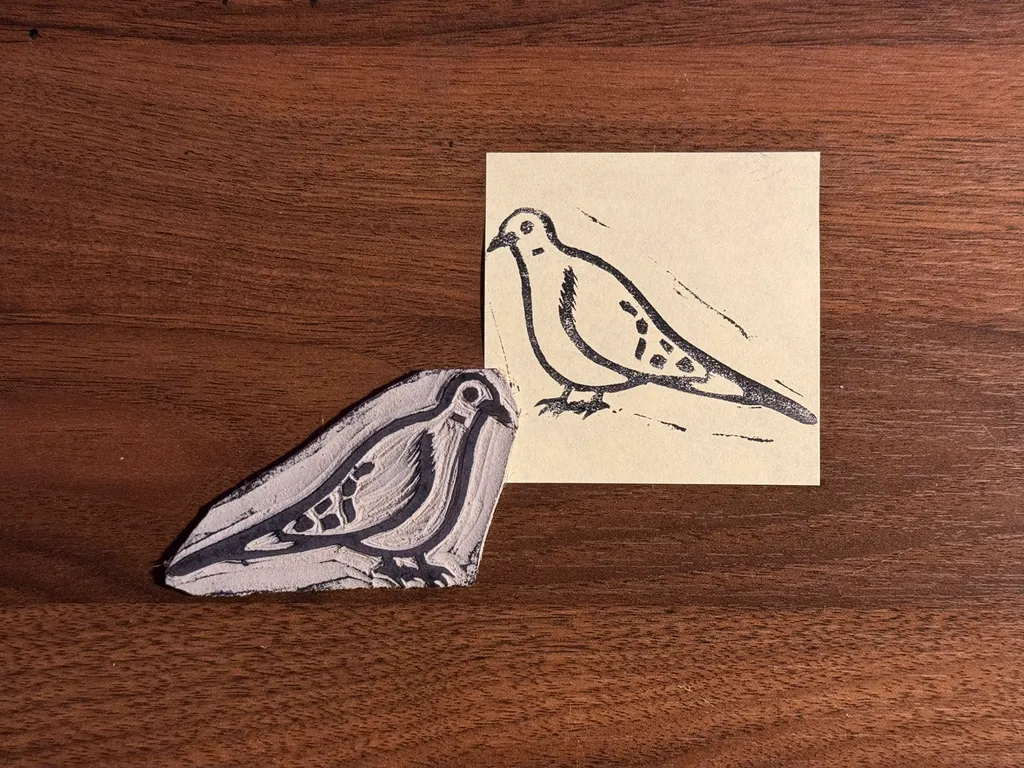 A light gray, textured sculpture of a bird rests on dark wood next to a beige card featuring a dark ink drawing of a stylized bird.