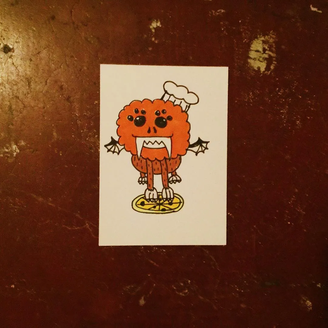 A cartoon orange pumpkin creature wearing a chef's hat and small black wings stands on a yellow plate, drawn on white paper set against a dark reddish-brown textured background.