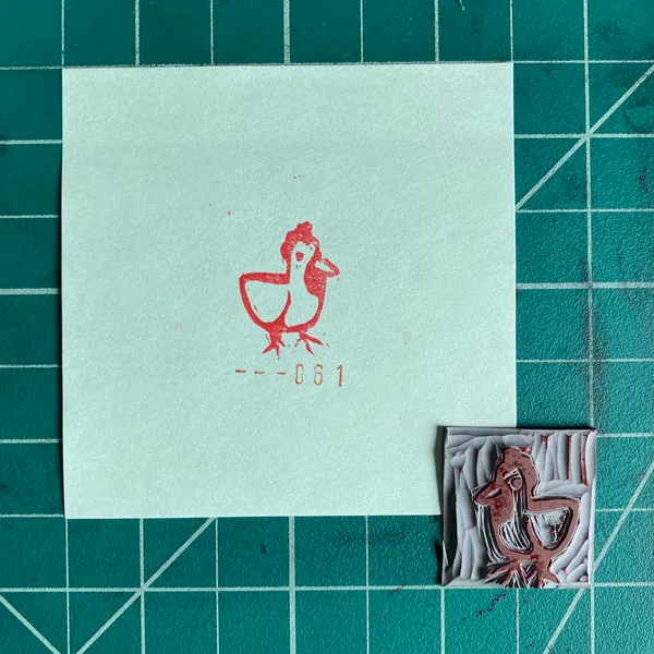 On a teal grid background, a light card displays a red printed duck and number 061, next to a small, textured square containing a raised reddish duck figure.