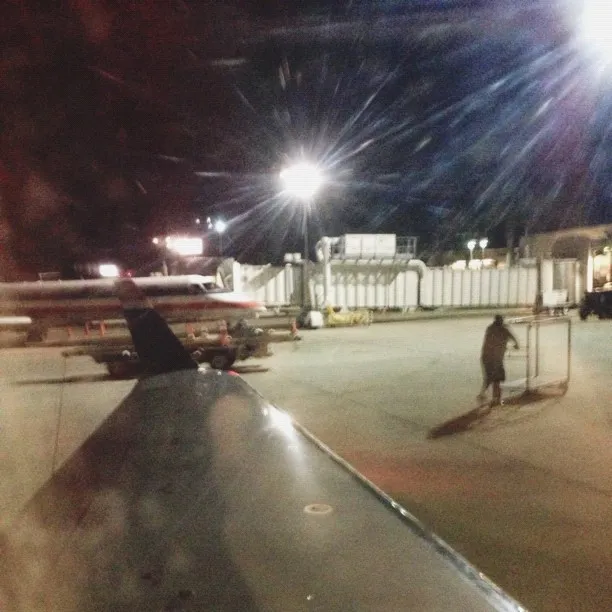 A curved, reflective metal surface dominates the foreground, leading to a dark, nighttime scene featuring bright artificial lights and distant structures.