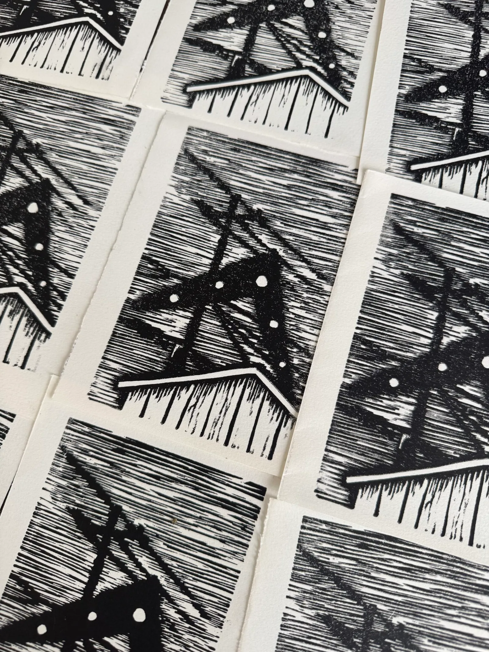 A grid of small, black and white prints featuring repeating geometric motifs of gabled houses and intersecting lines over a dense, horizontally striped background.