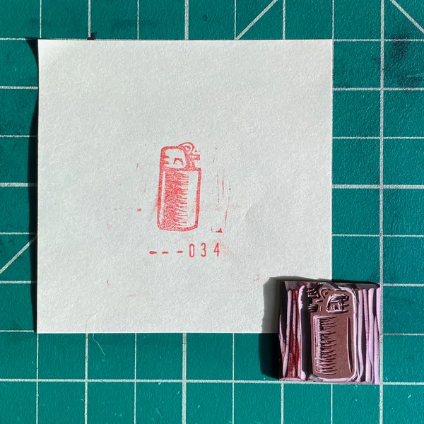 A white card on a teal grid displays a red outline drawing of a spray can and the numbers --034, positioned above a small stack of colored rectangles in shades of red and purple.