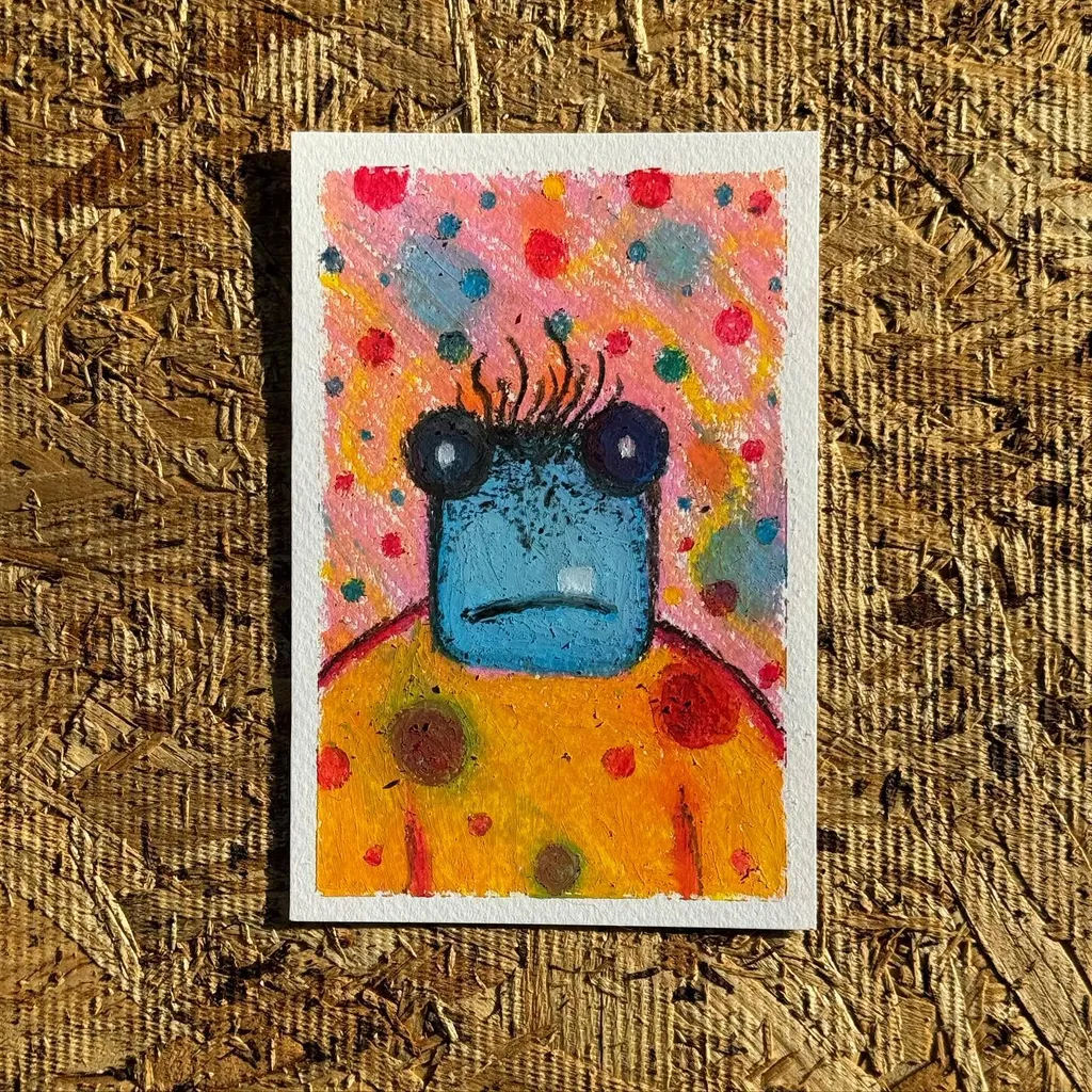 A stylized creature with a blue face and large eyes is centered against a colorful background speckled with red, blue, and yellow dots, wearing a yellow and orange patterned garment.