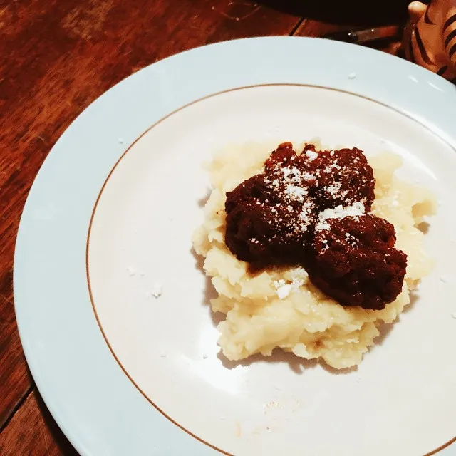 A mound of pale yellow mash and three dark, dense scoops rest on a white plate, dusted with white powder, set against a visible wooden background.