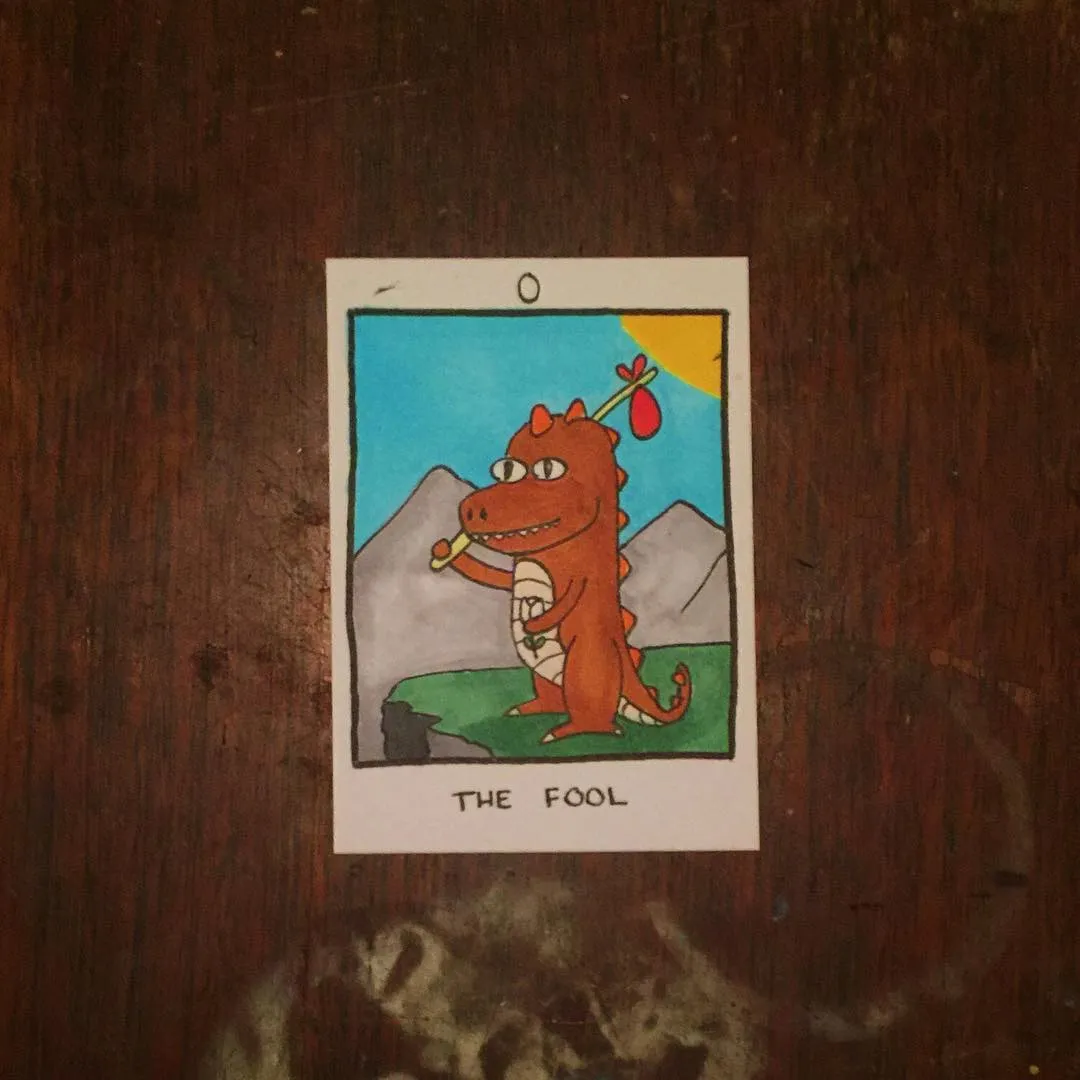 A cartoon reddish-orange dinosaur stands in a blue sky landscape with green ground and gray mountains, holding a red object and wearing a red decoration on its head.