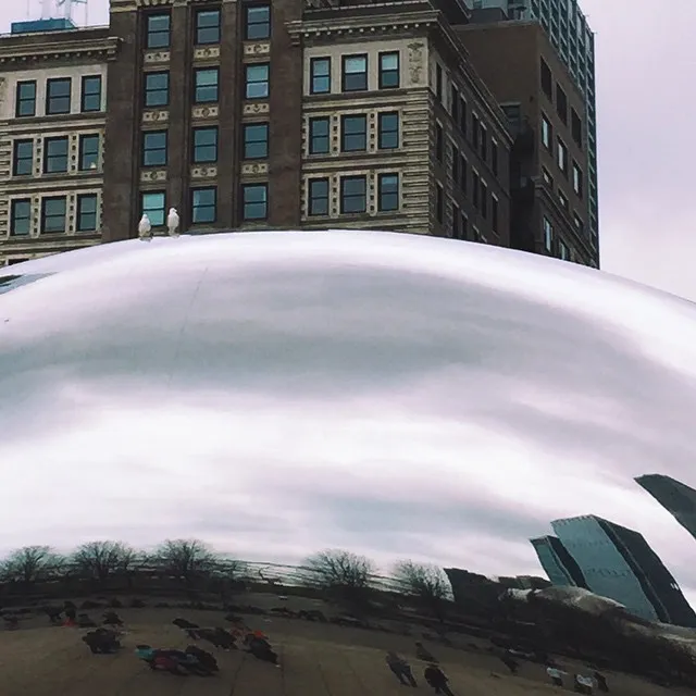 A massive, smooth white dome dominates the foreground, curving over a dark, grassy area, with a multi-story brick building visible behind it under an overcast sky.